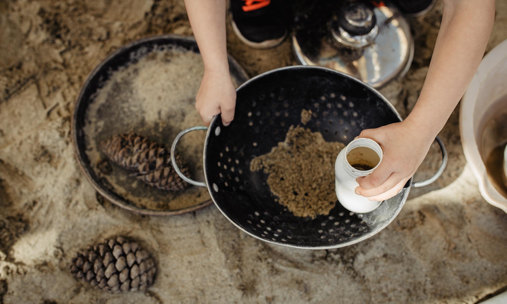 A child's hands sifting sand through a colander outdoors